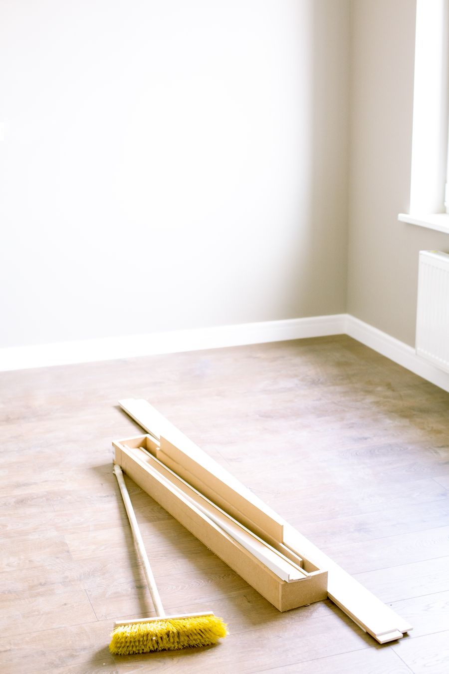 Empty room with new laminate flooring part-laid, a box of skirting and a broom