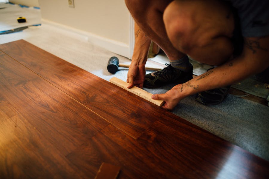 Person seating a laminate floorboard against the previous row using a tapping block and rubber mallet