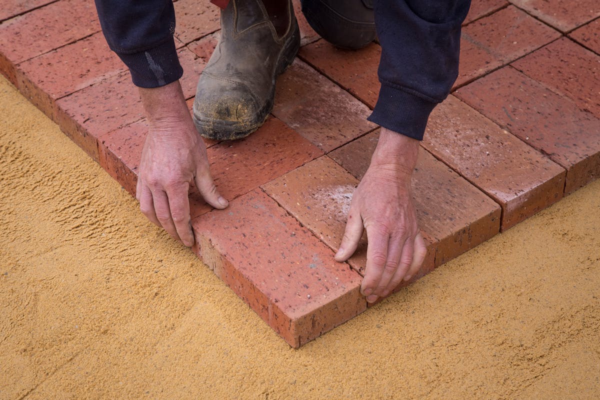 Worker laying clay pavers onto a screeded sand bed