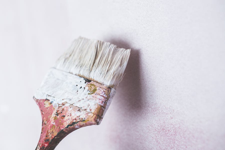 Close-up of an angled brush cutting in a clean band of white paint along a wall edge