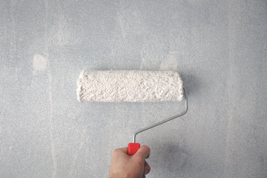 Hand rolling white paint onto an interior wall with a paint roller
