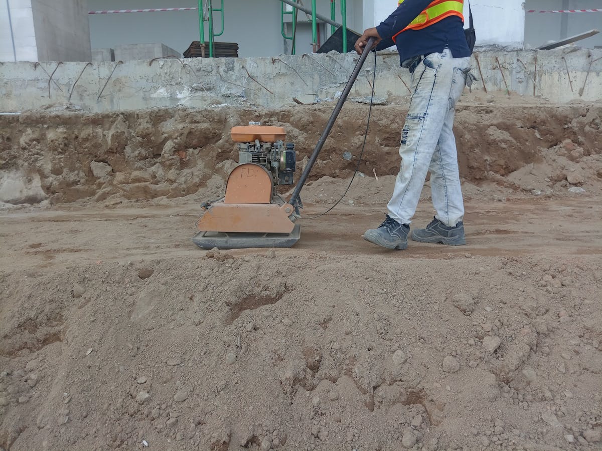 Worker compacting a base with a plate compactor before laying pavers