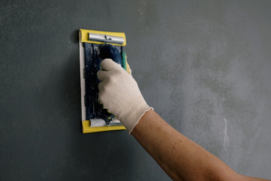 Person scraping a grey interior wall with a putty knife to remove flaking paint