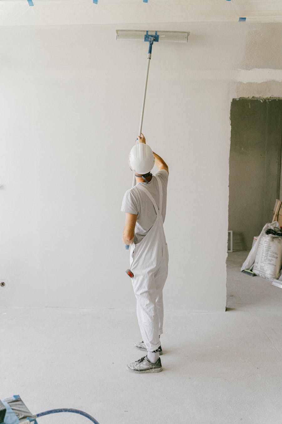 Back view of a person coating a wall with a brush and roller