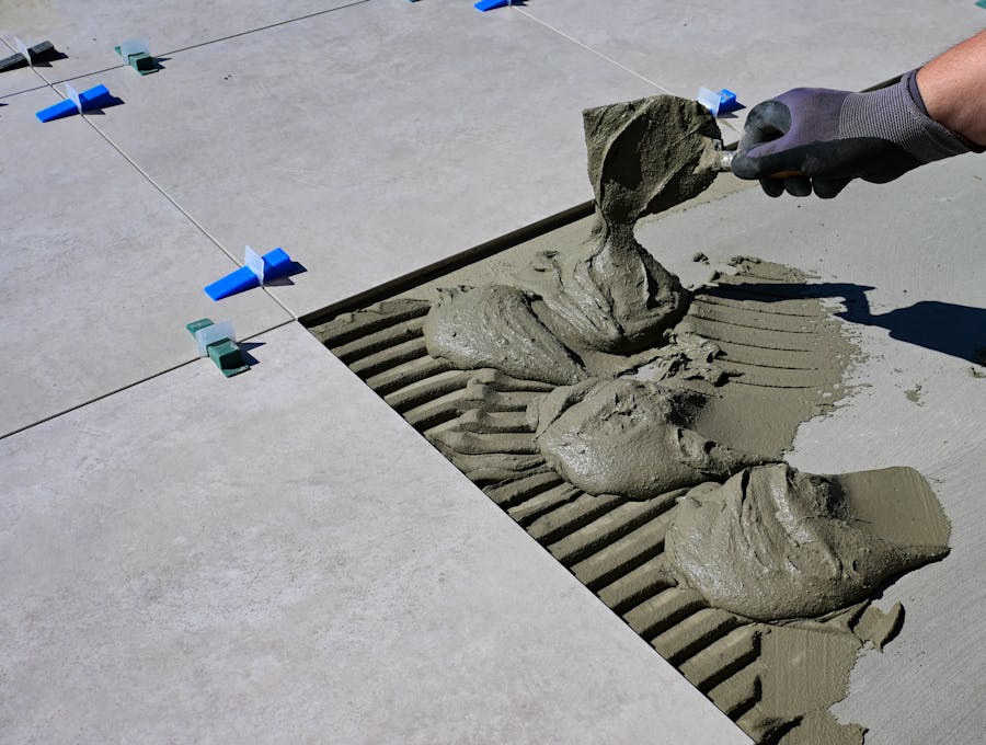Gloved hand combing out grey adhesive with a notched trowel, tile levelling clips visible alongside
