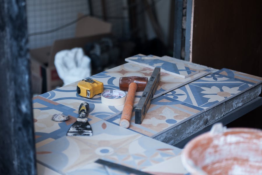 Tiling tools laid out on a bench, including a rubber mallet, level, putty knife and tape measure